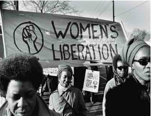 Black feminists holding up a banner that reads WOMENS LIBERATION at a Womens March.